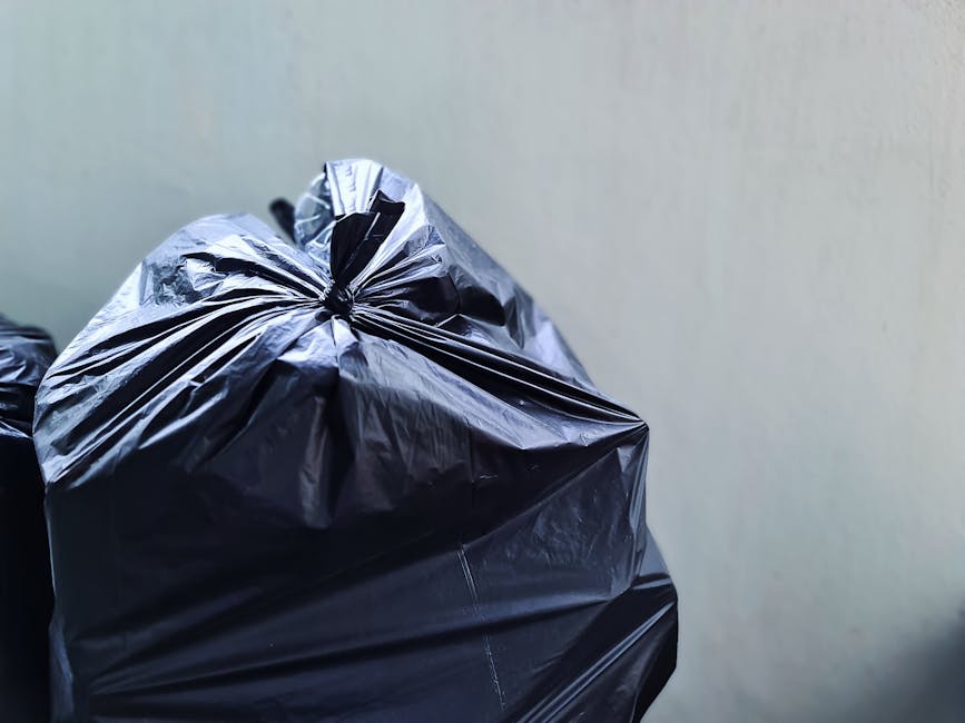 A pile of discarded waste materials is situated on a paved outdoor area adjacent to a brick and concrete wall. The debris includes a wooden garden bed or shelving unit with slatted panels stacked at a